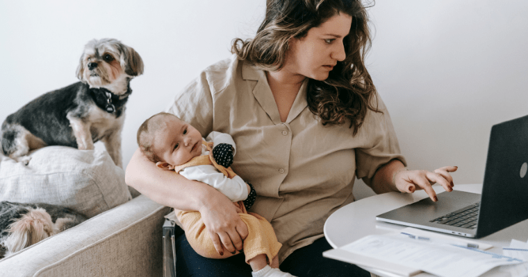 Mãe trabalhando em casa no computador enquanto cuida do bebê, representando a estabilidade no emprego durante o Auxílio Maternidade.